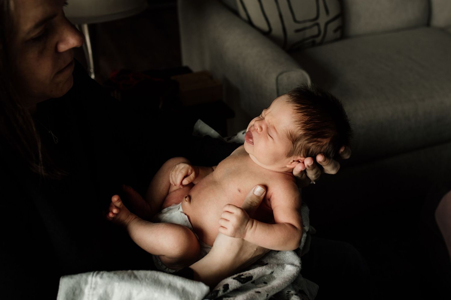 Newborn baby lies unclothed in a peaceful sleep while being held in dimly lit room.