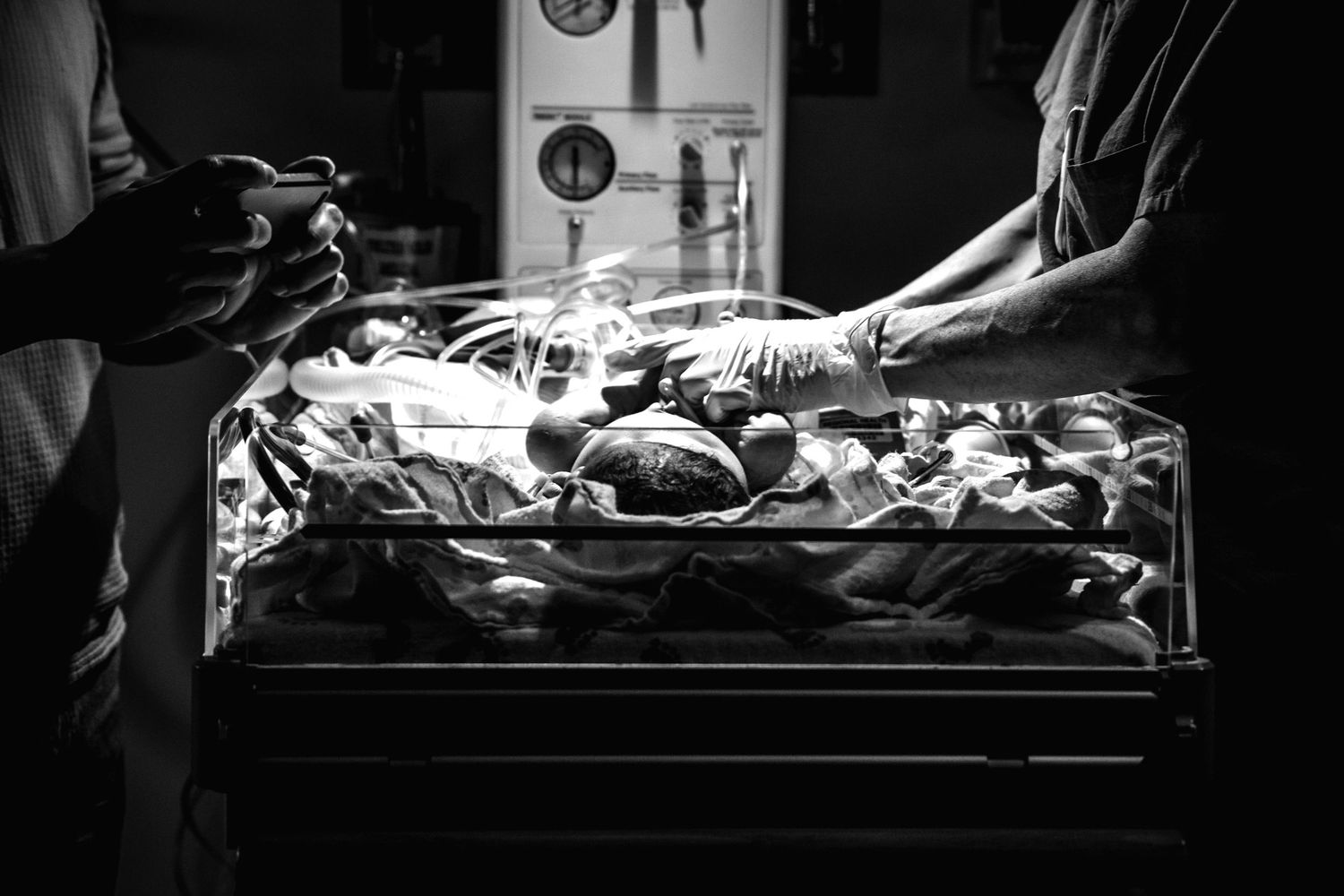 Newborn baby under warming lights in a hospital bassinet attended by medical staff.