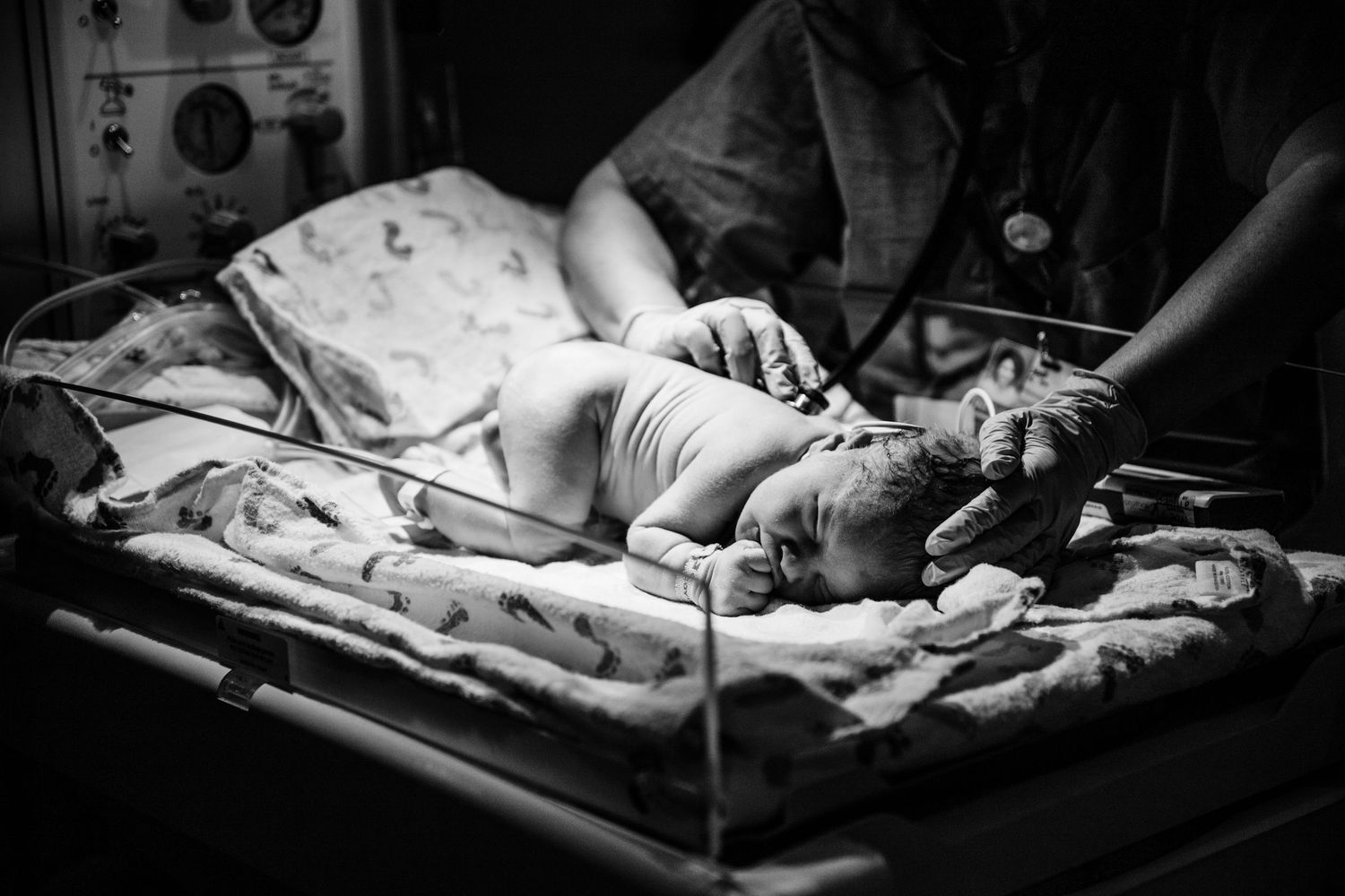 Black and white photo of newborn baby being examined by medical staff in hospital nursery.
