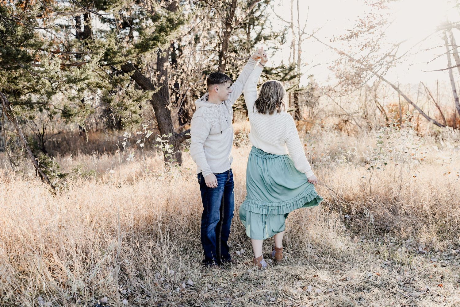 Couple walking hand in hand through a sunlit autumn field surrounded by tall golden grasses.