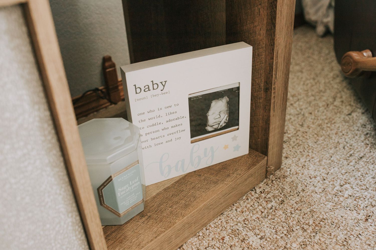 Baby sonogram photo displayed in a wooden shelf frame with a candle in a nursery.