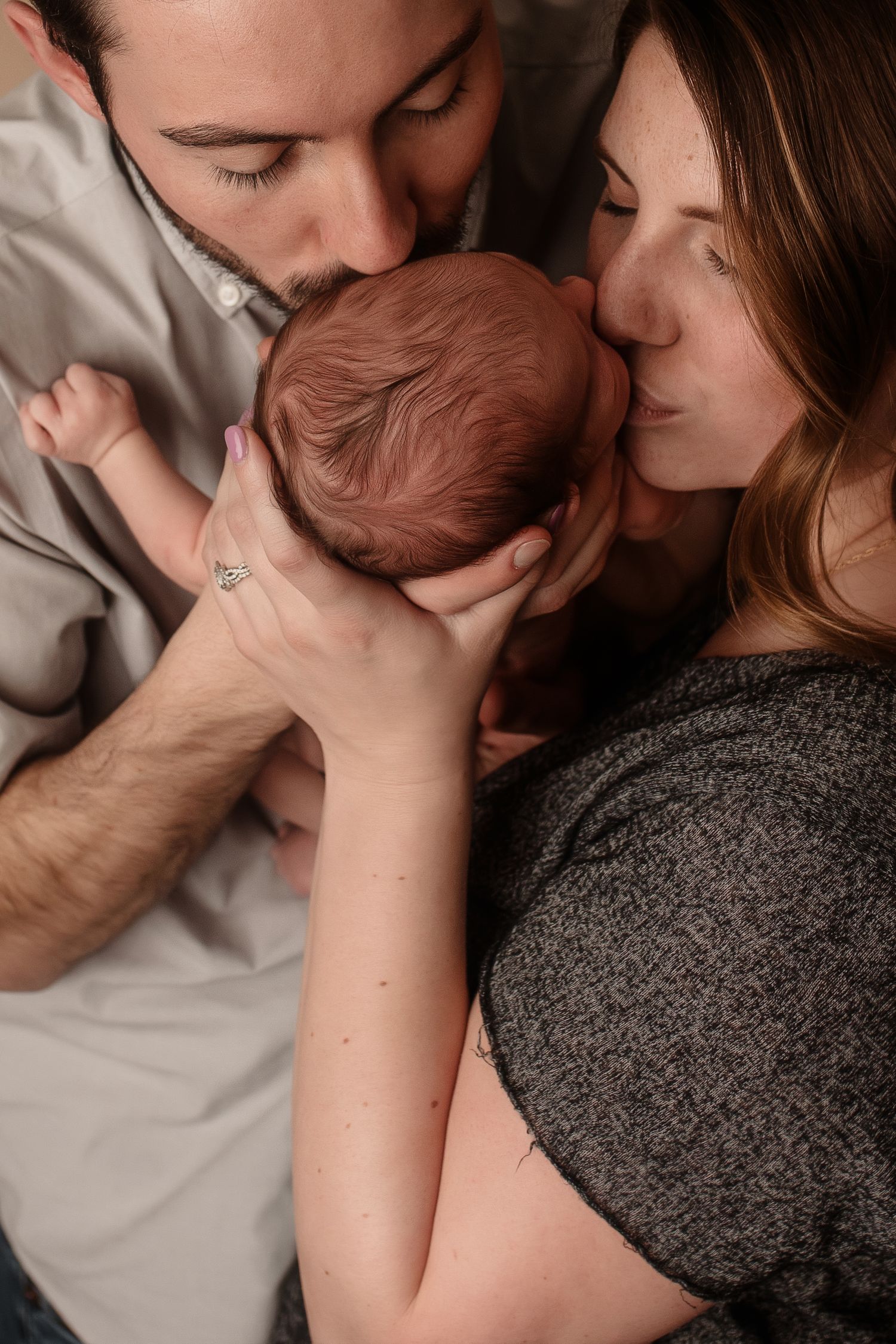 Loving parents kissing their newborn baby on the head in a tender family portrait.