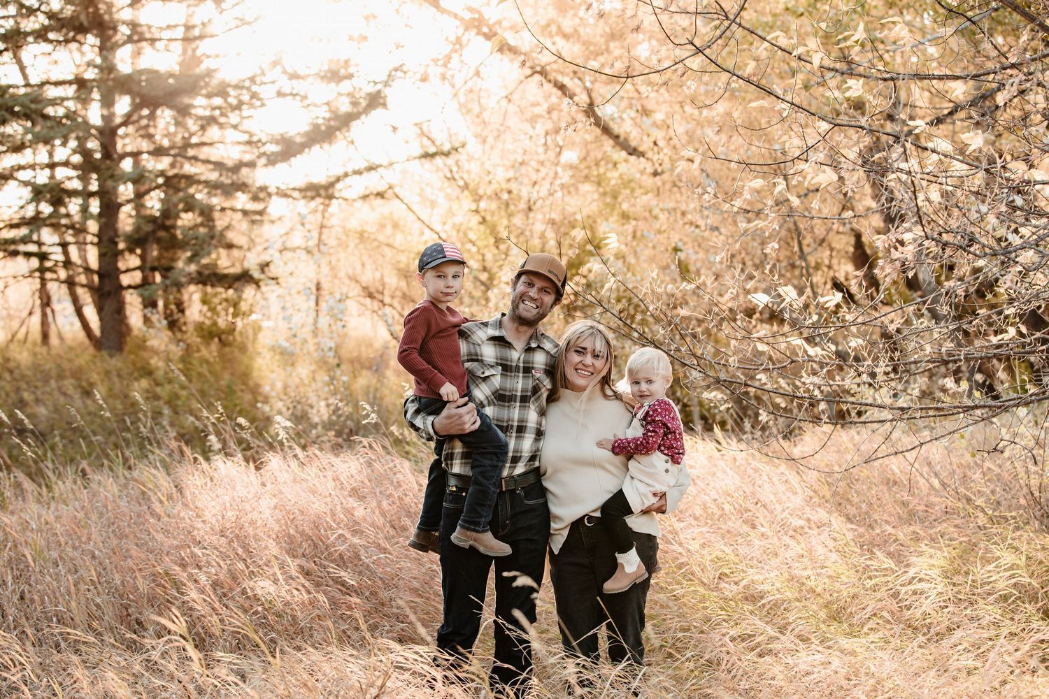 A family enjoys a stroll together through tall autumn grasses and flowering trees on a golden afternoon.