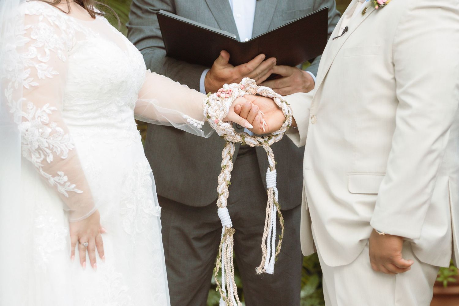 Bride and groom hands bound together with braided cord during a handfasting wedding ceremony.
