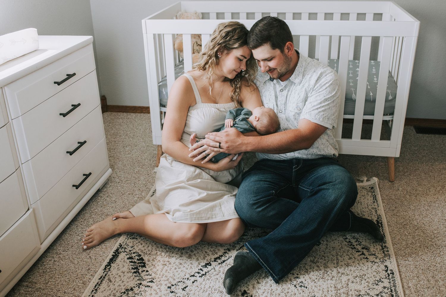 New parents sitting on nursery floor together lovingly holding their newborn baby.
