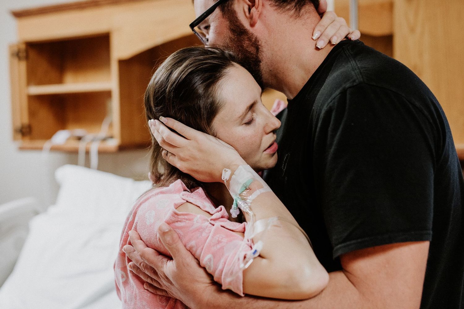 Couple sharing emotional embrace in hospital room after childbirth.
