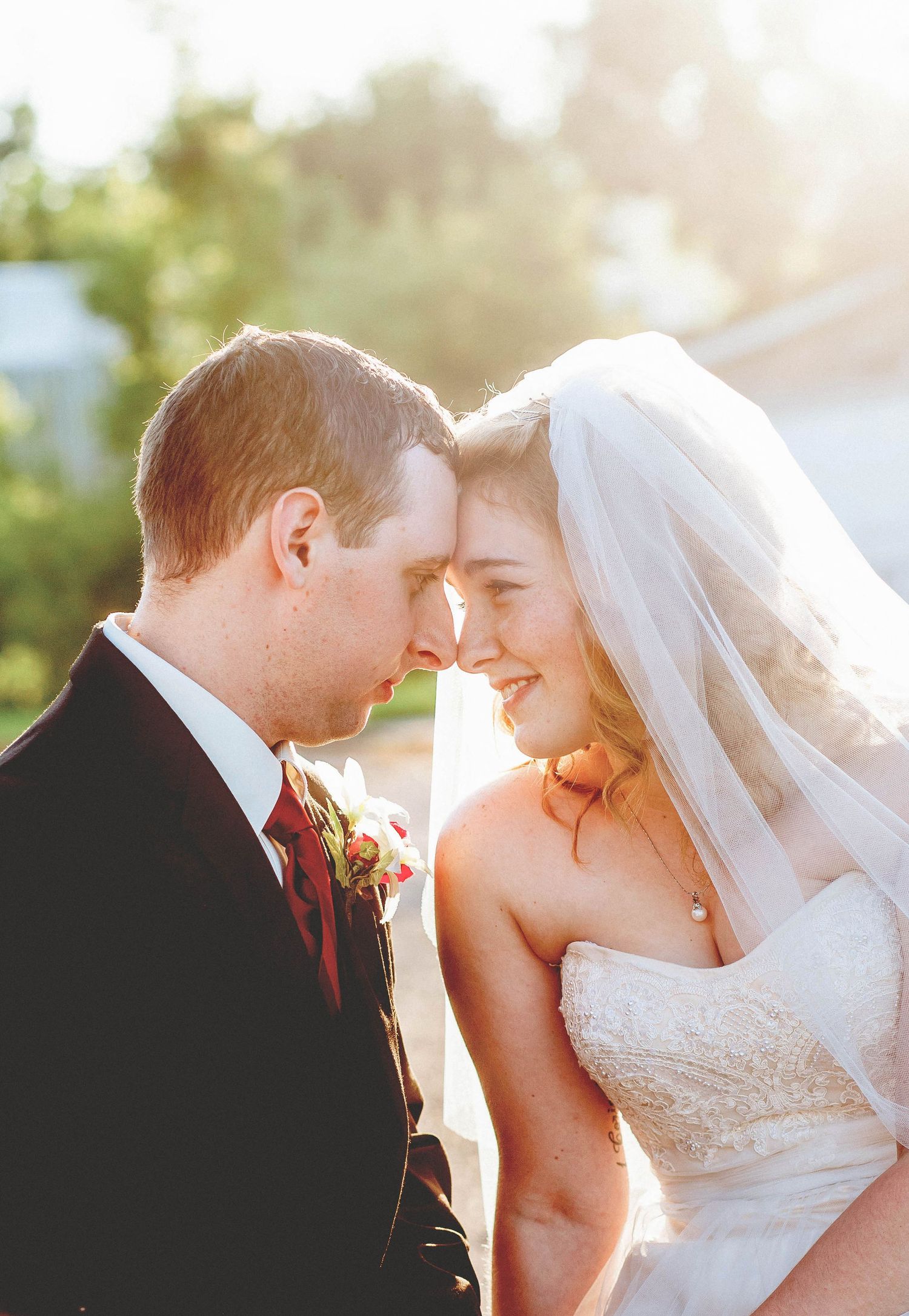 A bride and groom touch foreheads tenderly in golden sunlight, sharing an intimate romantic moment on their wedding day.