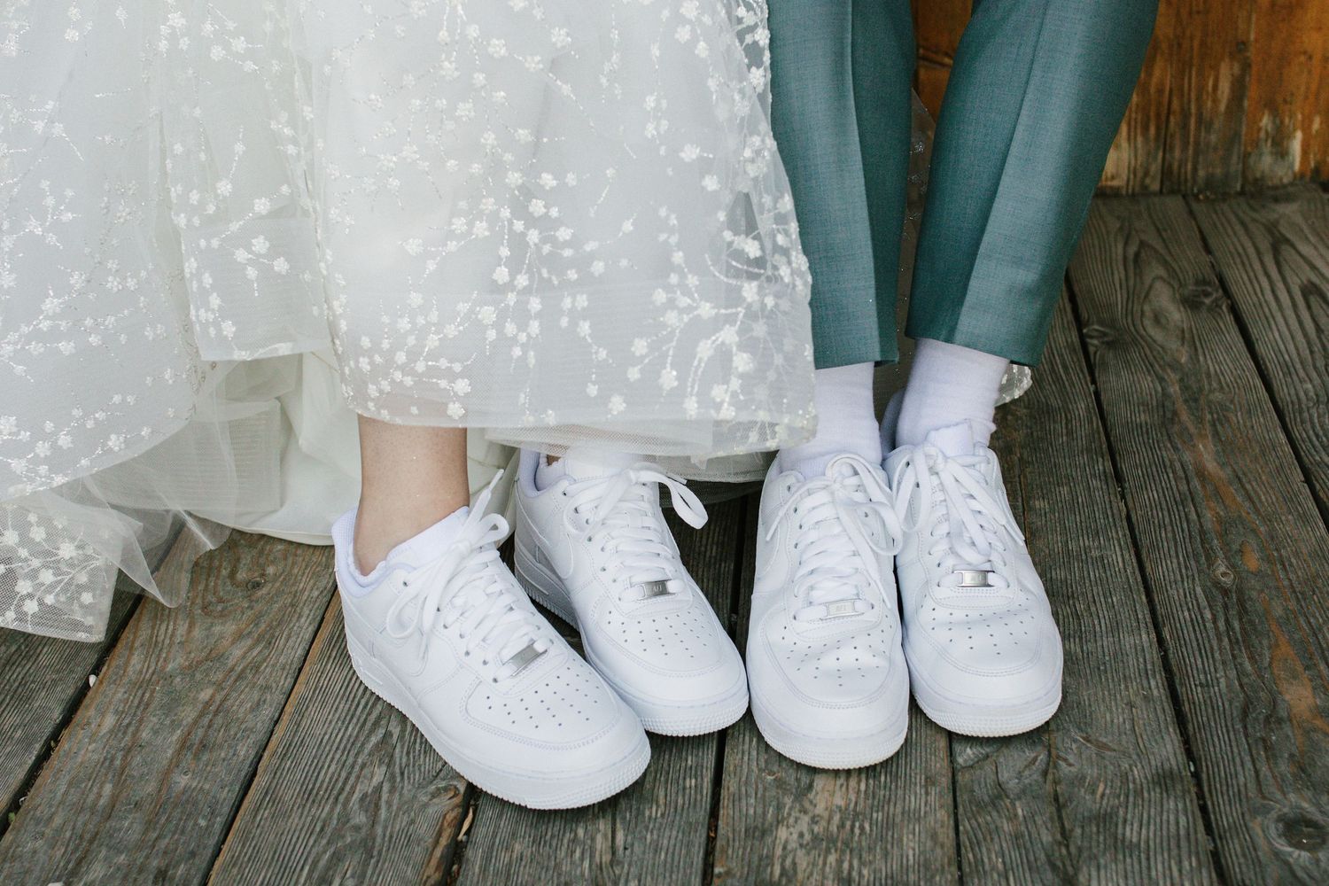 Bride and groom wearing matching white Nike Air Force 1 sneakers on wooden deck at wedding.