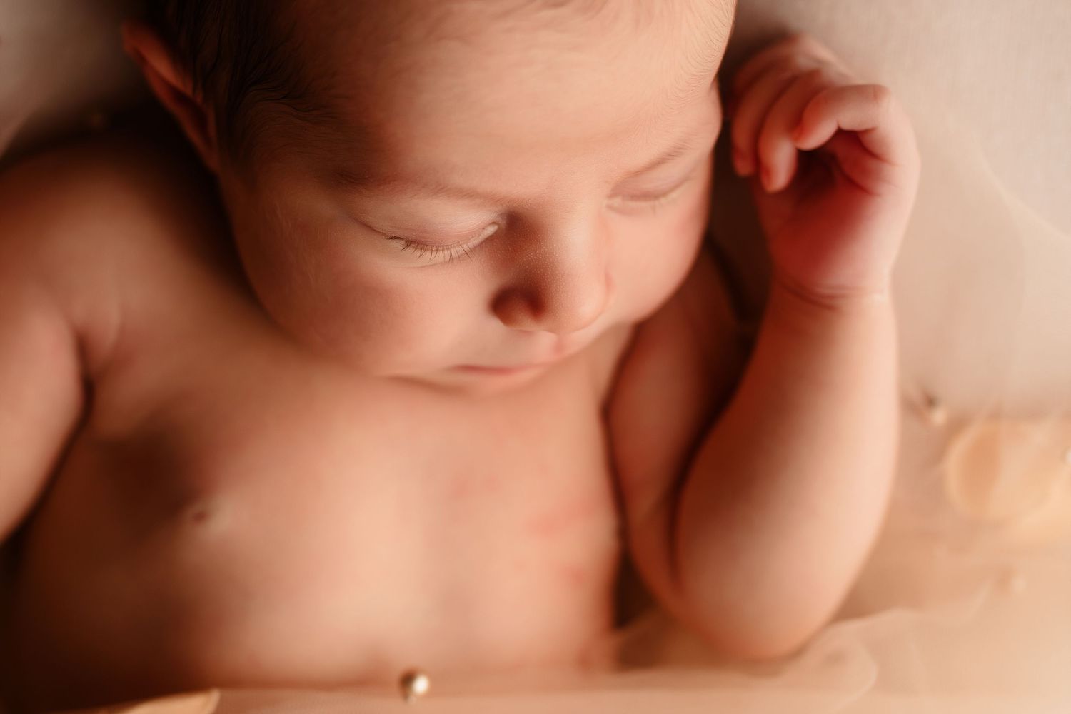 Serene sleeping newborn baby lying on cream fabric with delicate gold bracelet detail.