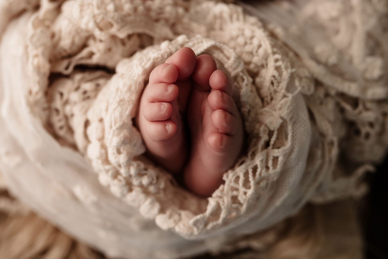 Tiny newborn baby toes and feet wrapped in cream knit lace blanket close-up.