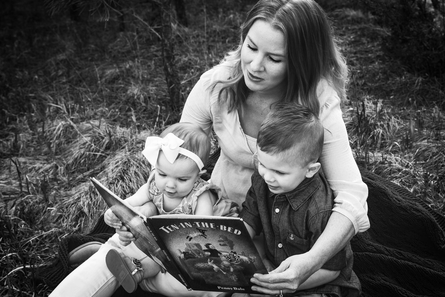 Mother reads a book with her two young children outdoors in nature.