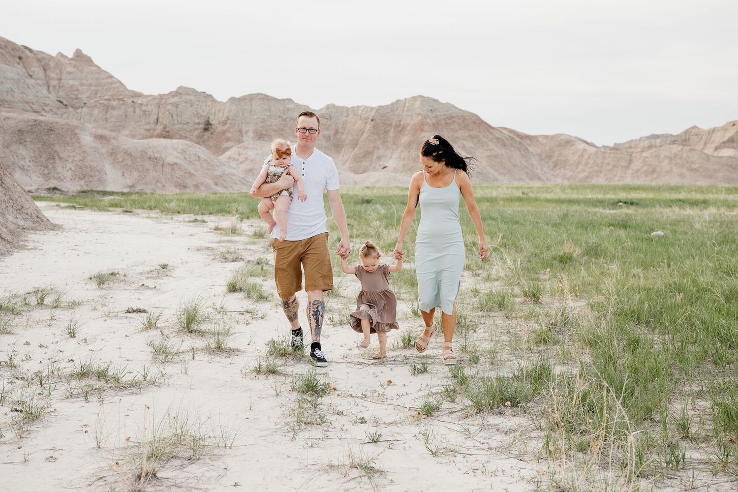 Happy family of four walking through sandy badlands landscape with two young children.