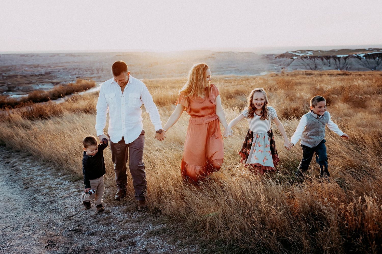 Happy family of five holding hands while walking along a path in a golden field.