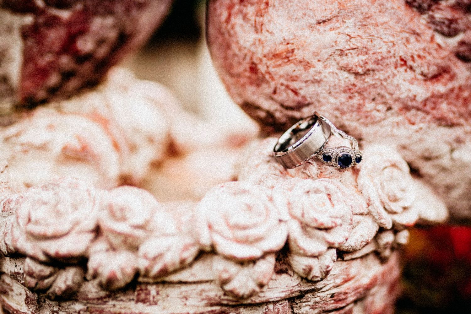 Two silver rings with dark gemstones resting on a decorative pink floral ceramic sculpture.