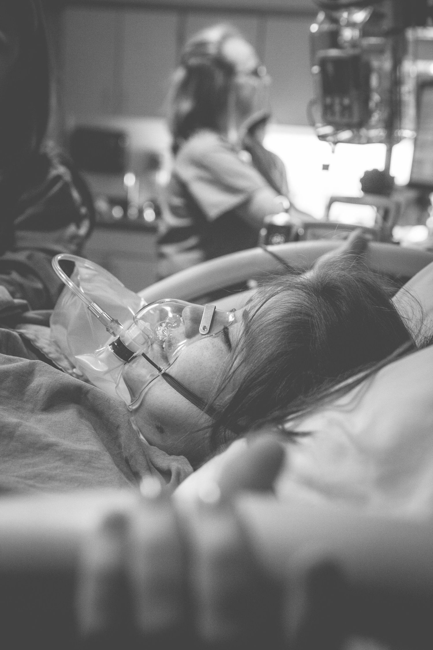 Black and white photo of a patient lying in a hospital bed wearing an oxygen mask during labor.