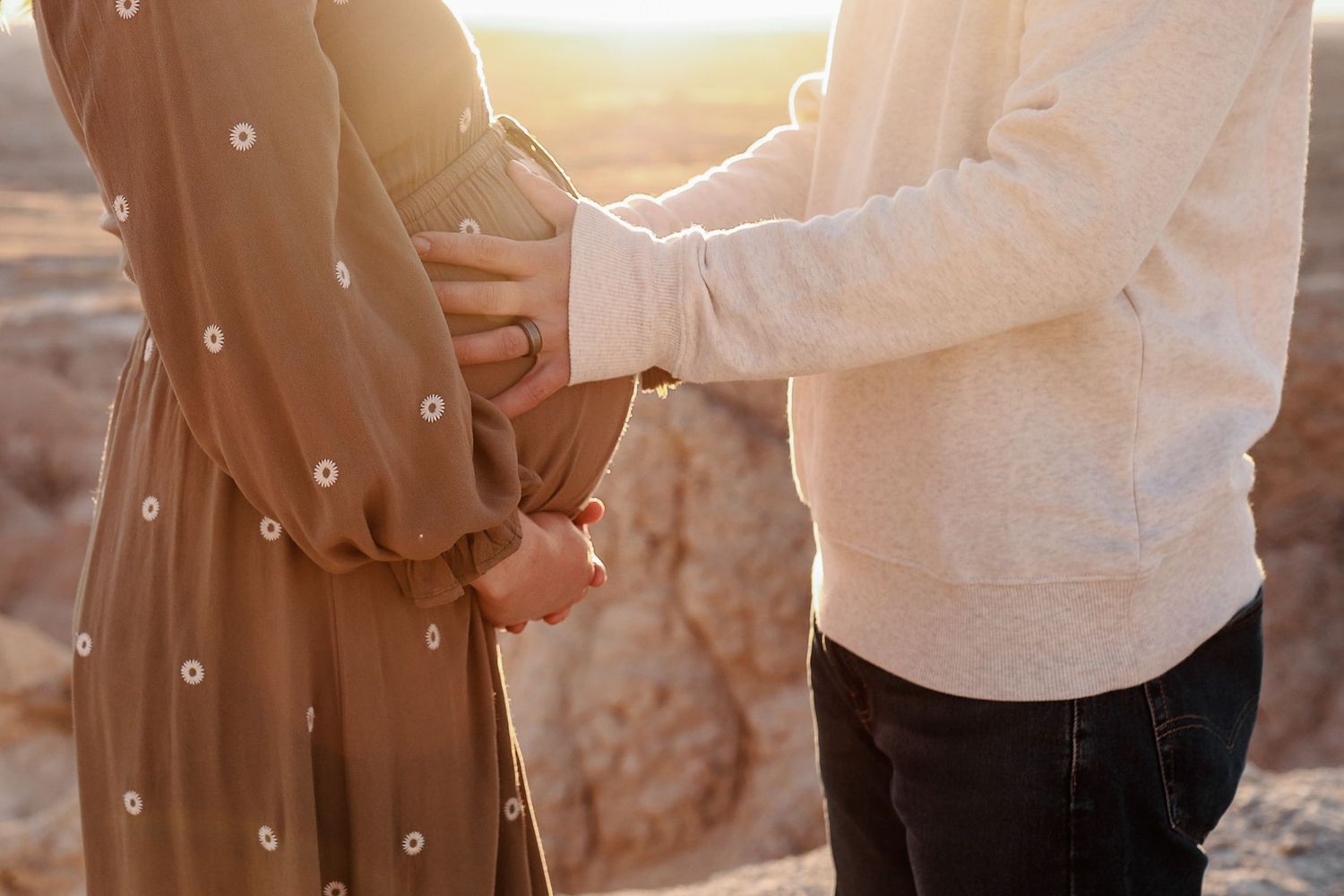 Couple holding hands at sunset, pregnant woman in floral dress with partner.
