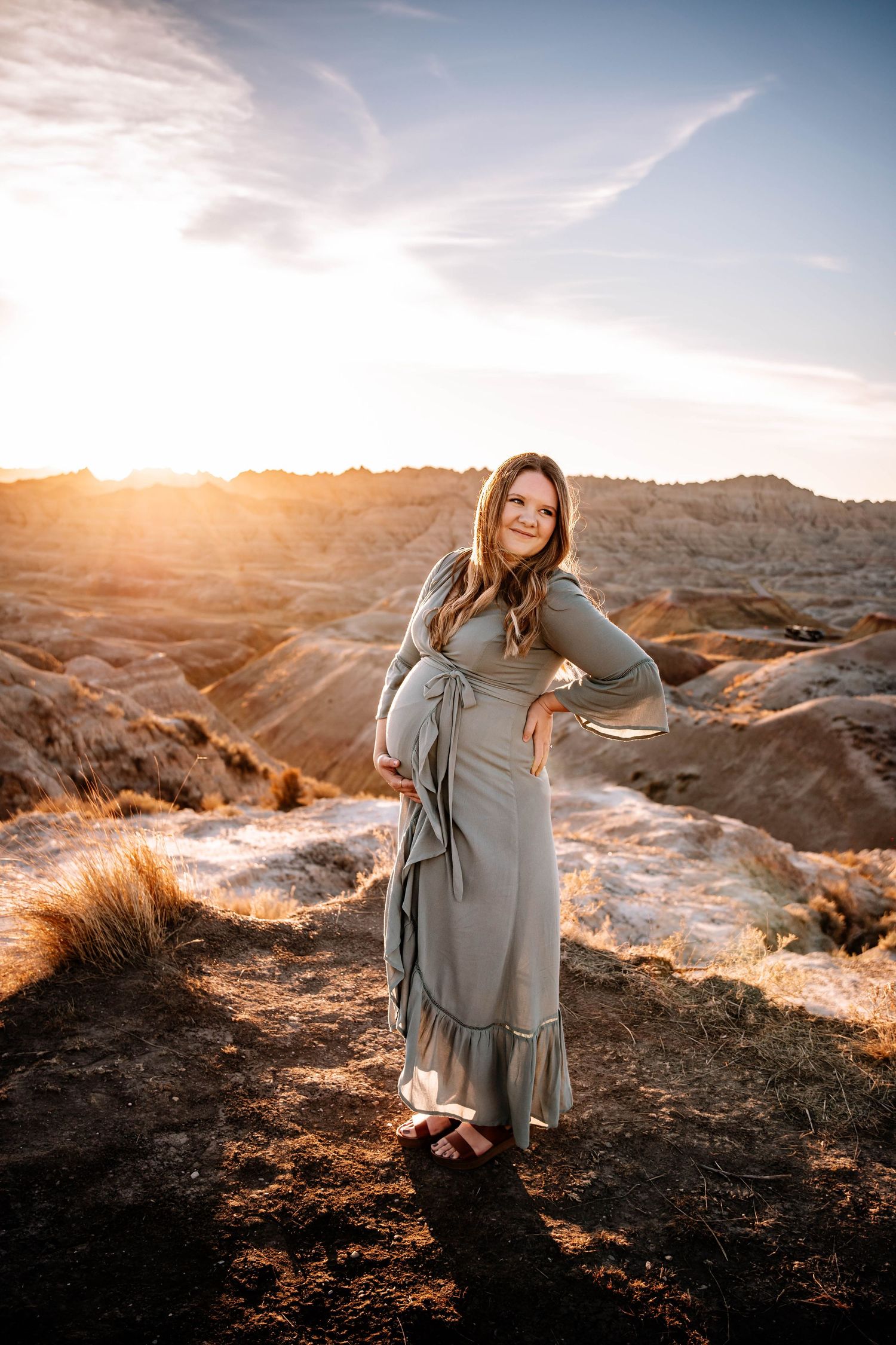 Pregnant woman in sage green maxi dress standing at golden hour in the Badlands.