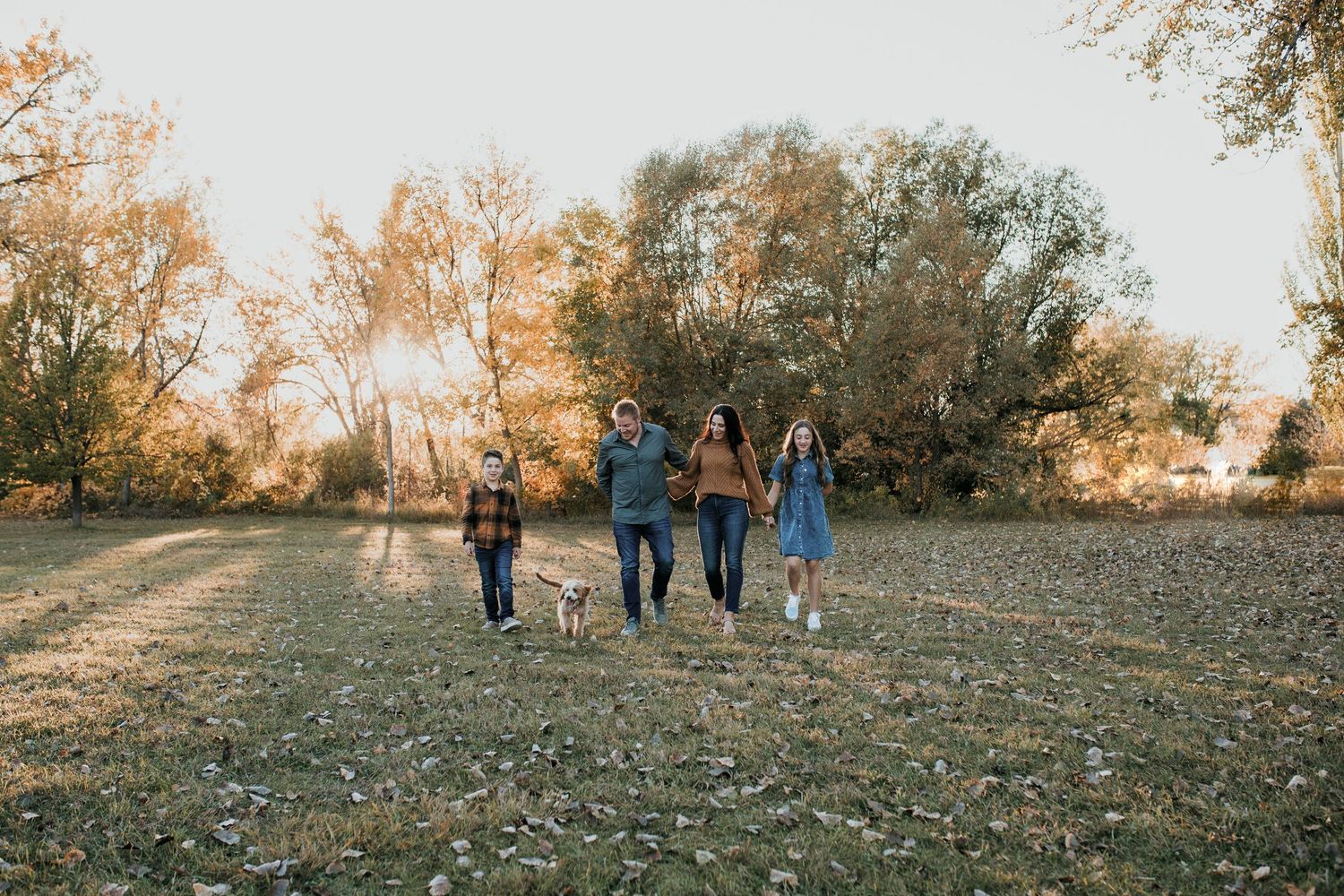 Family walking together in a field during golden sunset hour with fall foliage in background.