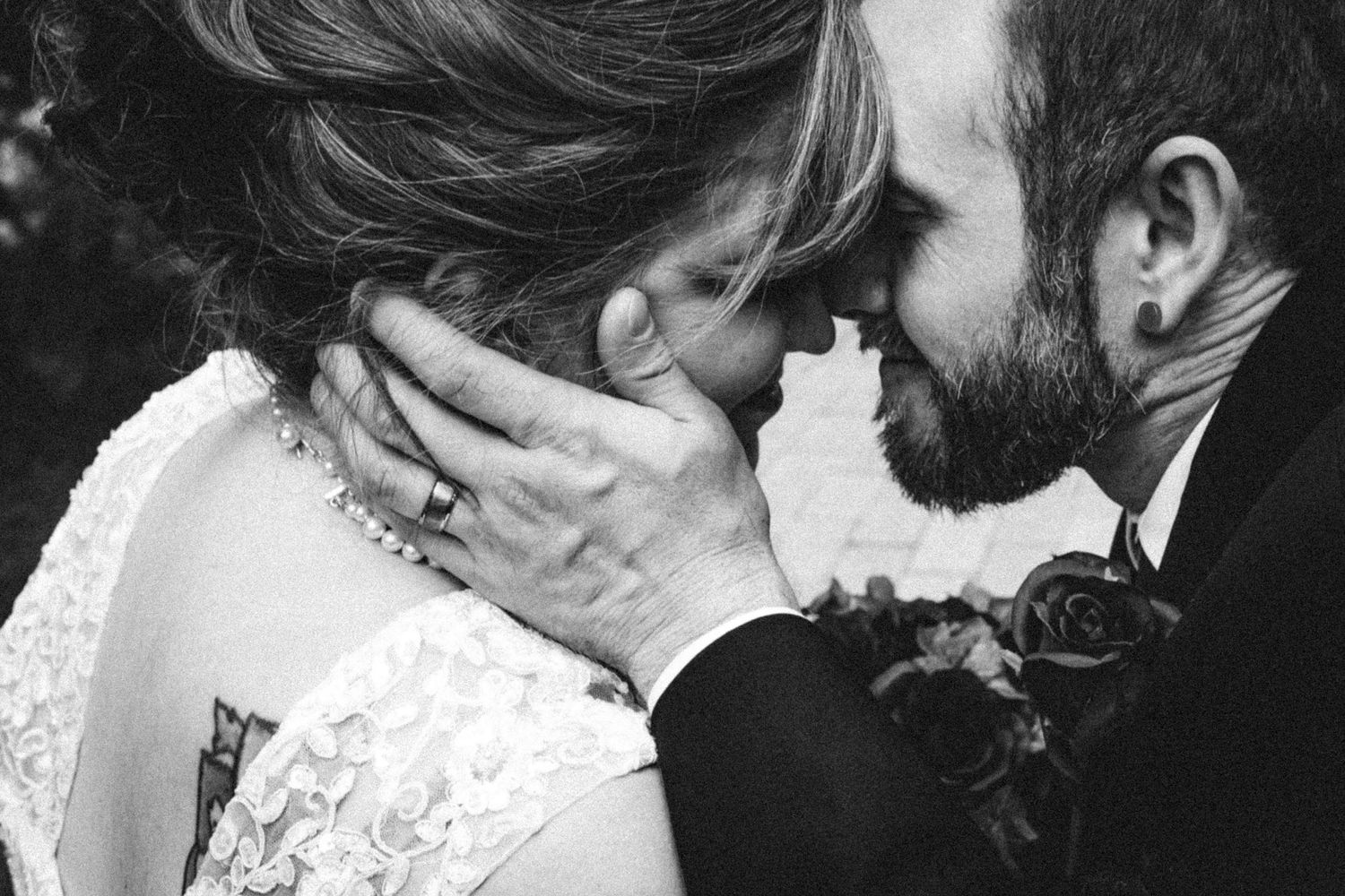 Black and white wedding photo of bride and groom sharing an intimate moment, groom tenderly holding brides face.