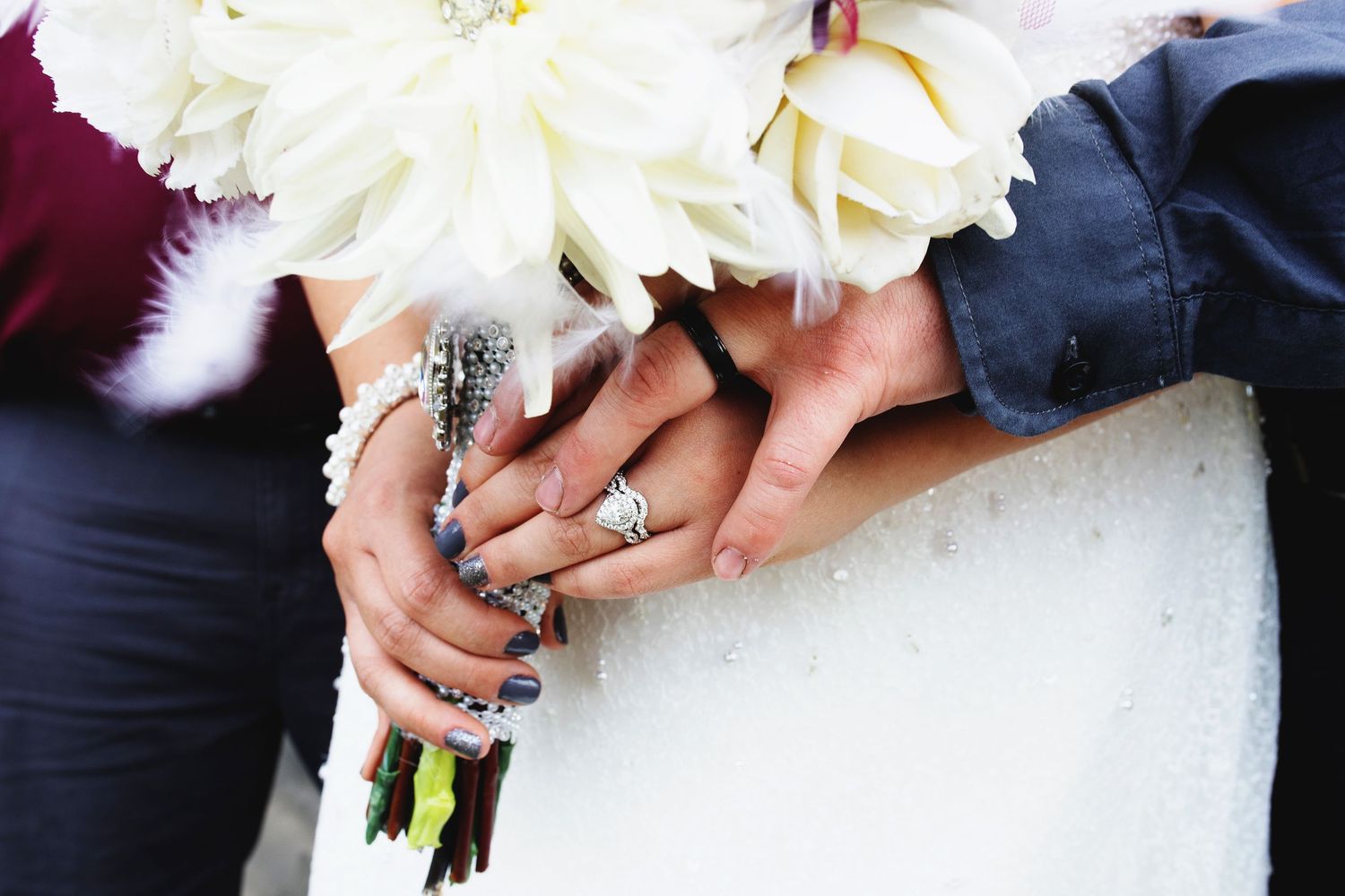 Close-up of bride holding white floral bouquet with diamond engagement ring and blue nail polish at wedding ceremony.