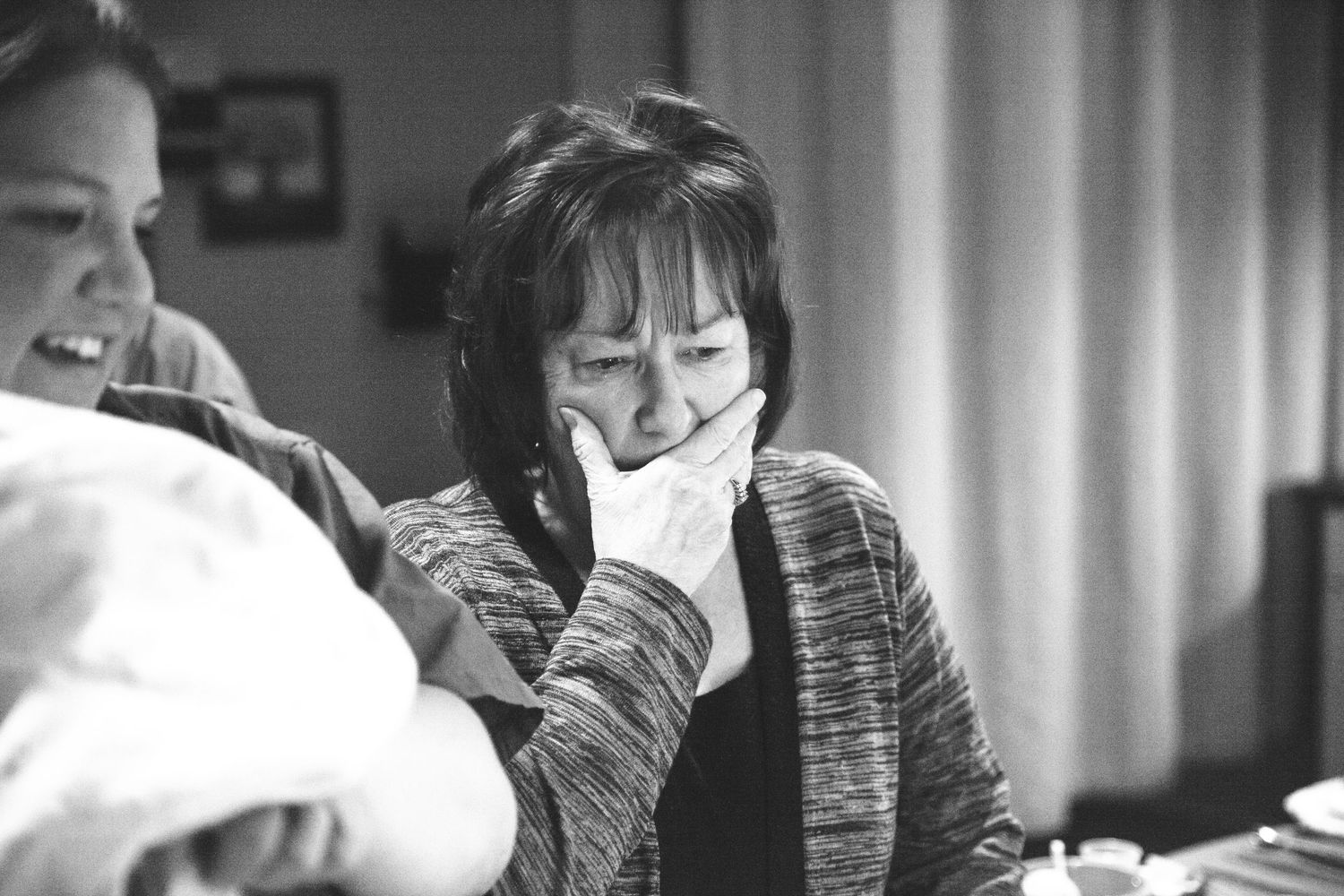 Emotional grandmother covers mouth while meeting newborn baby for first time, black and white photo.