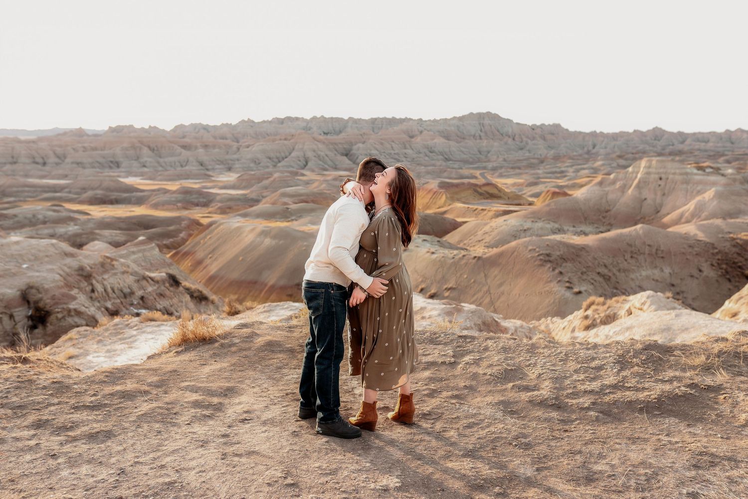 Couple sharing a romantic kiss in the scenic Badlands landscape at sunset.