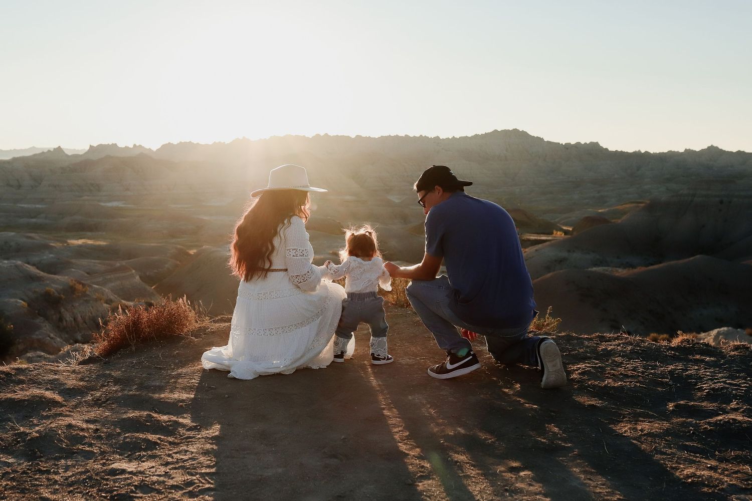 Parents with toddler enjoying golden sunset in vast desert badlands landscape, family photo session.