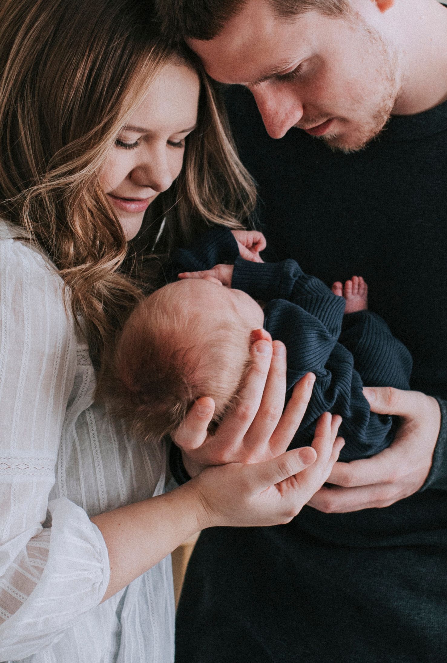 New parents lovingly cradling their sleeping newborn baby wrapped in a navy blue swaddle blanket.