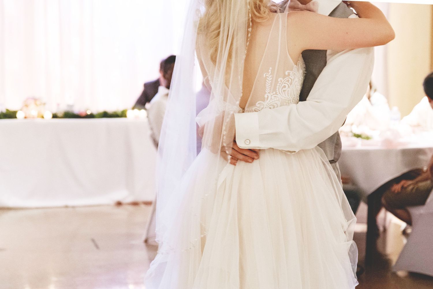 Bride and groom share their first dance, bride wearing elegant backless white wedding gown with veil.