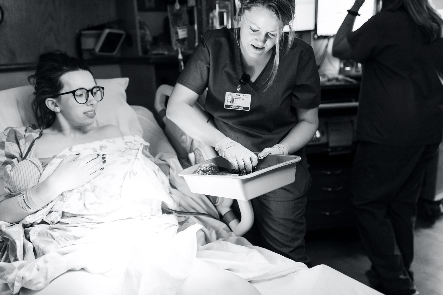 A black and white photograph shows a patient in bed receiving medical care from a nurse in a hospital setting.