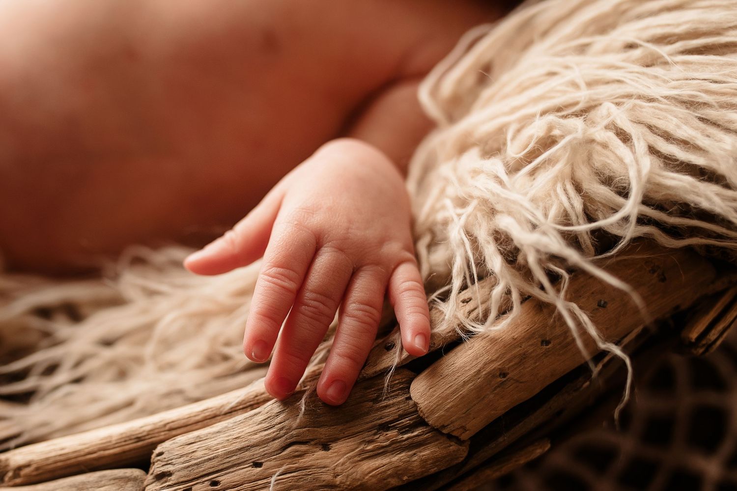 Close-up of newborn baby tiny hand resting on rustic driftwood with burlap texture.