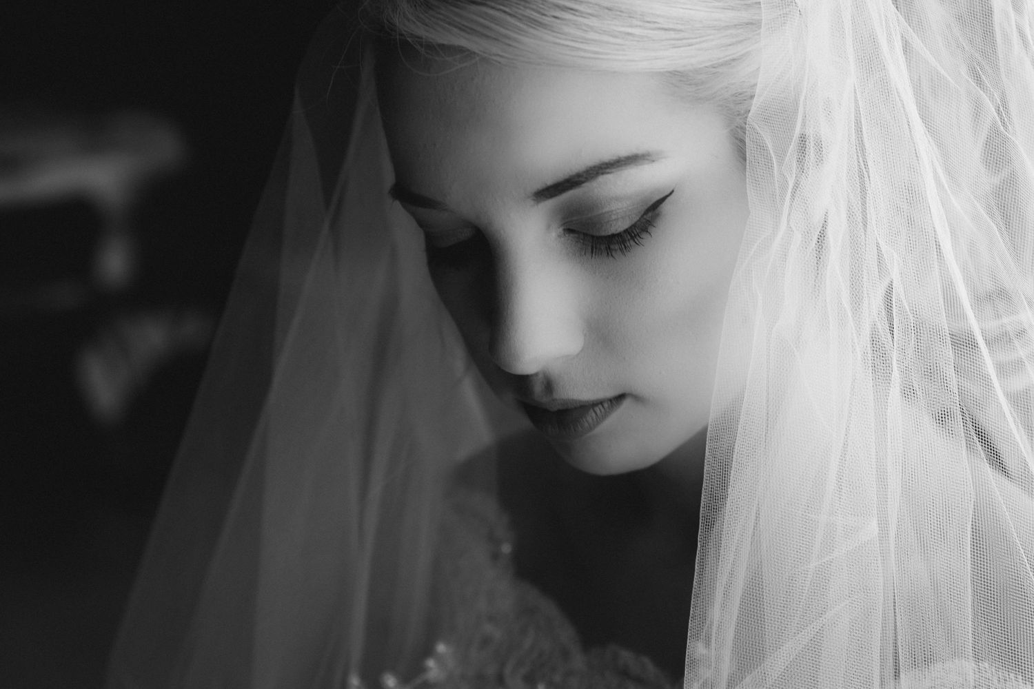 Black and white portrait of a blonde bride wearing a veil, looking down with elegant makeup on her wedding day.