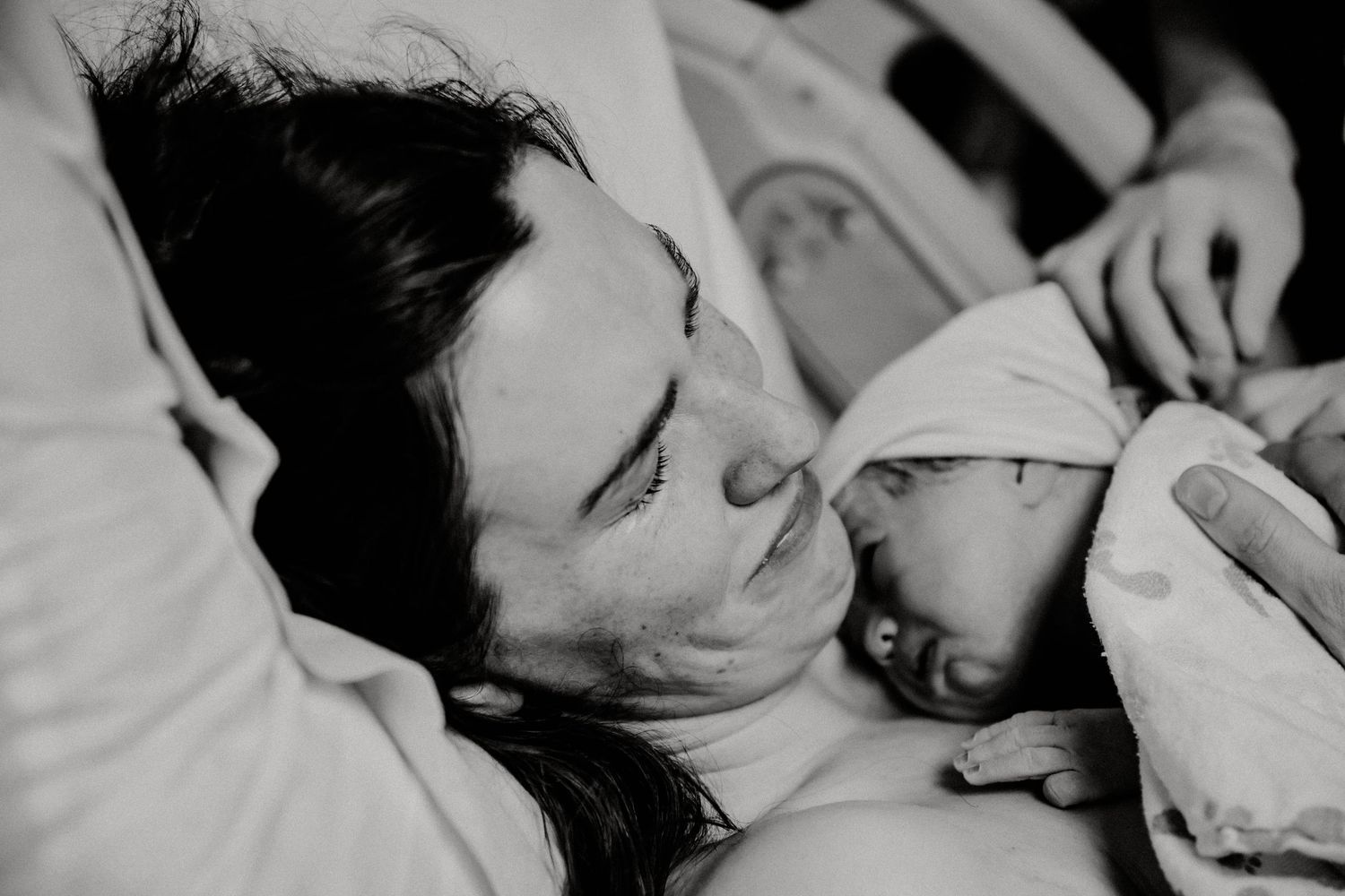 Black and white photo of exhausted mother smiling at her newborn after birth.