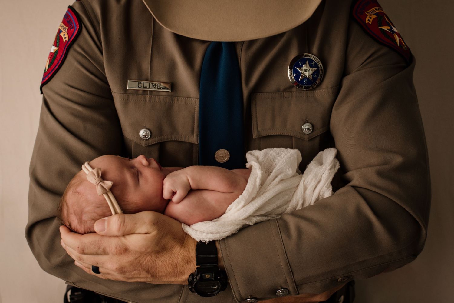 Texas state trooper in uniform gently cradling a sleeping newborn baby in their arms.