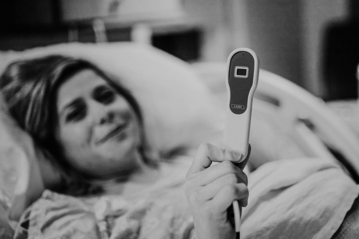 Black and white photo of a pregnant woman in hospital bed holding a medical call button device.