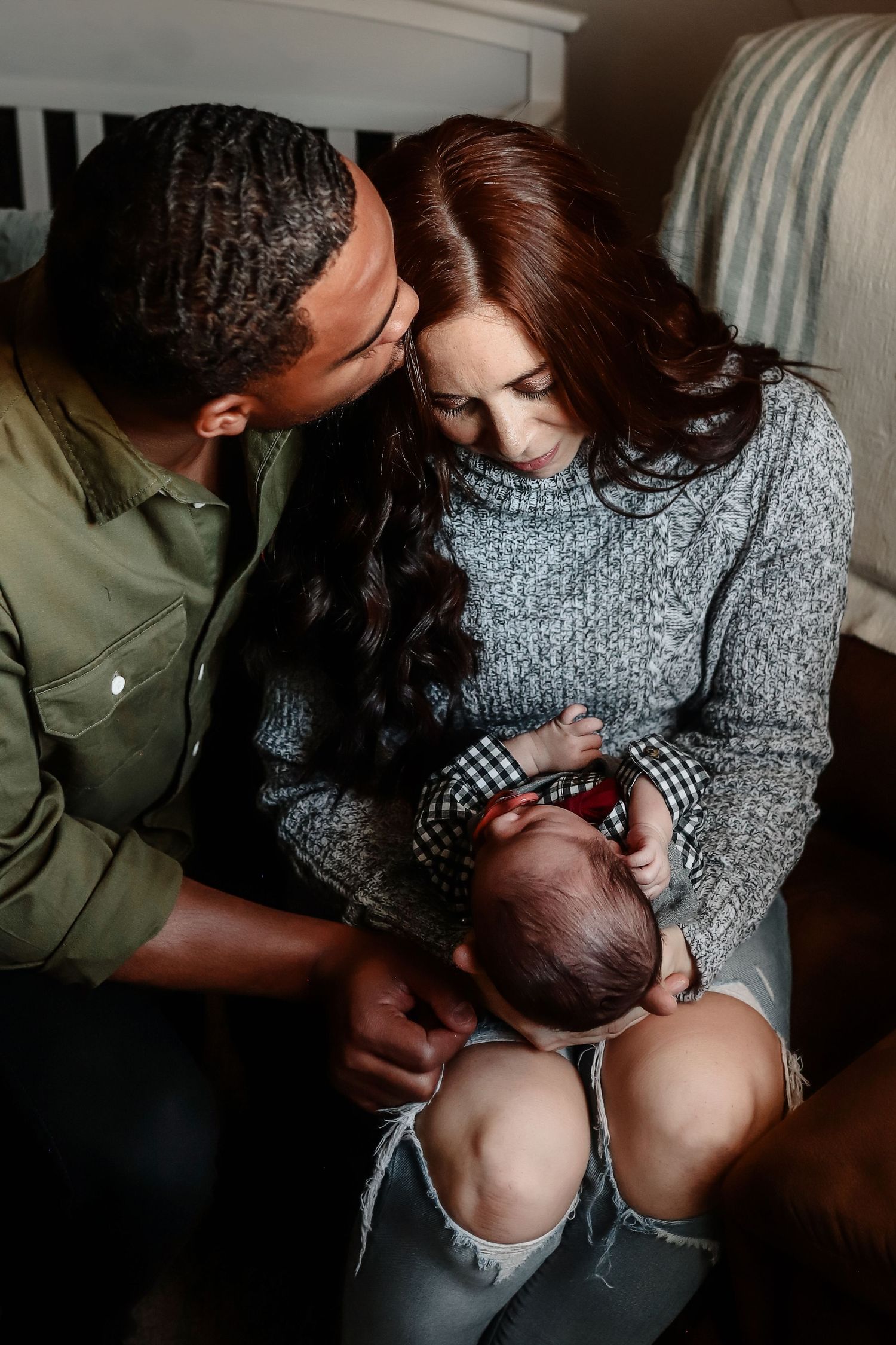 Loving parents together admiring their newborn baby in a softly lit nursery setting.