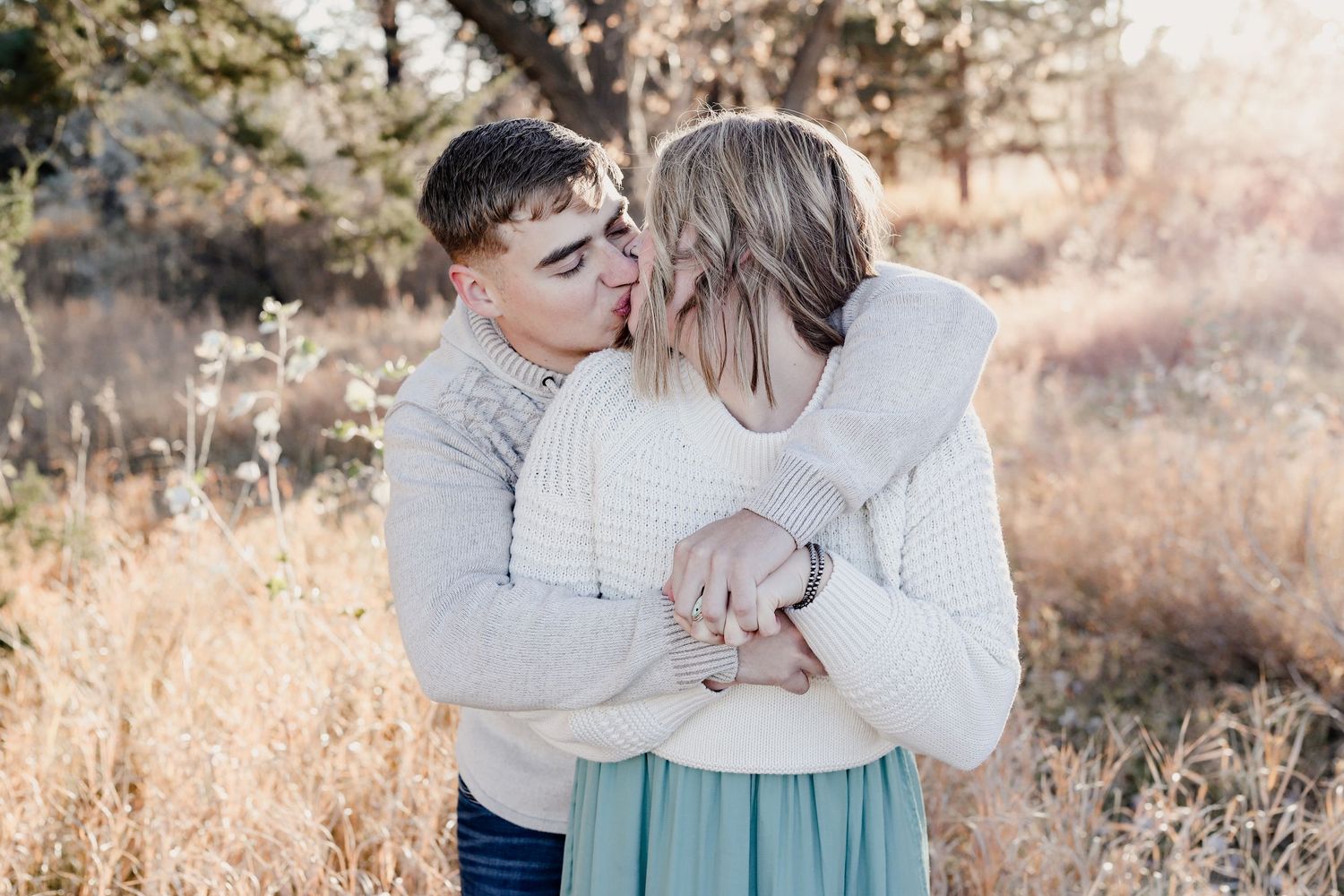 Young couple sharing a tender embrace in a golden autumn field during an outdoor photo session.