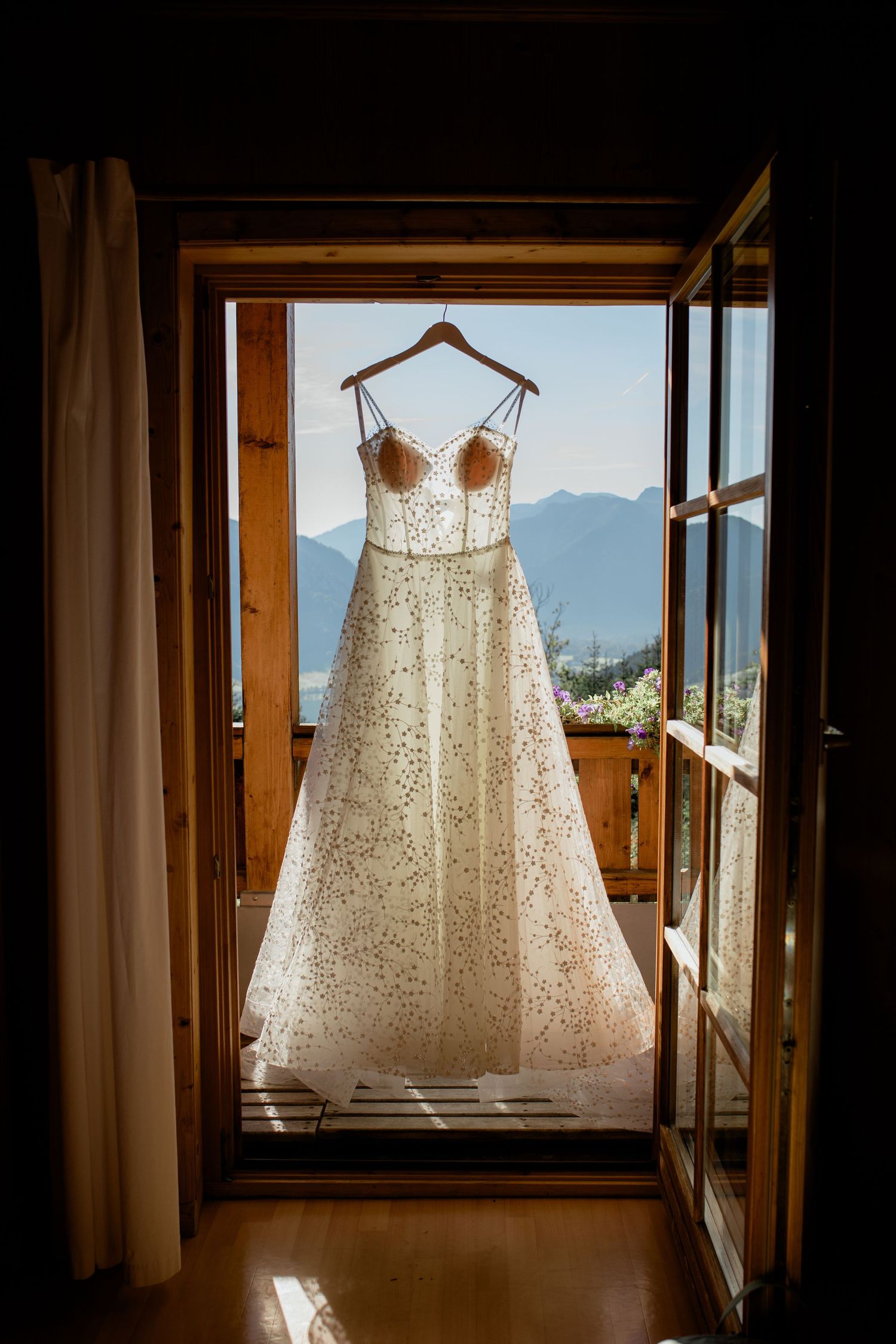 Elegant wedding dress hanging on a wooden balcony door with mountain views.
