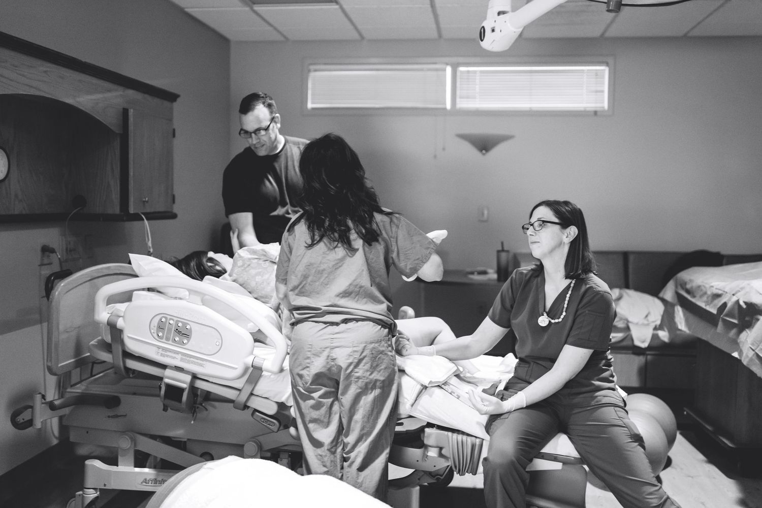 Medical team assists woman during labor in hospital delivery room, black and white birth photography.