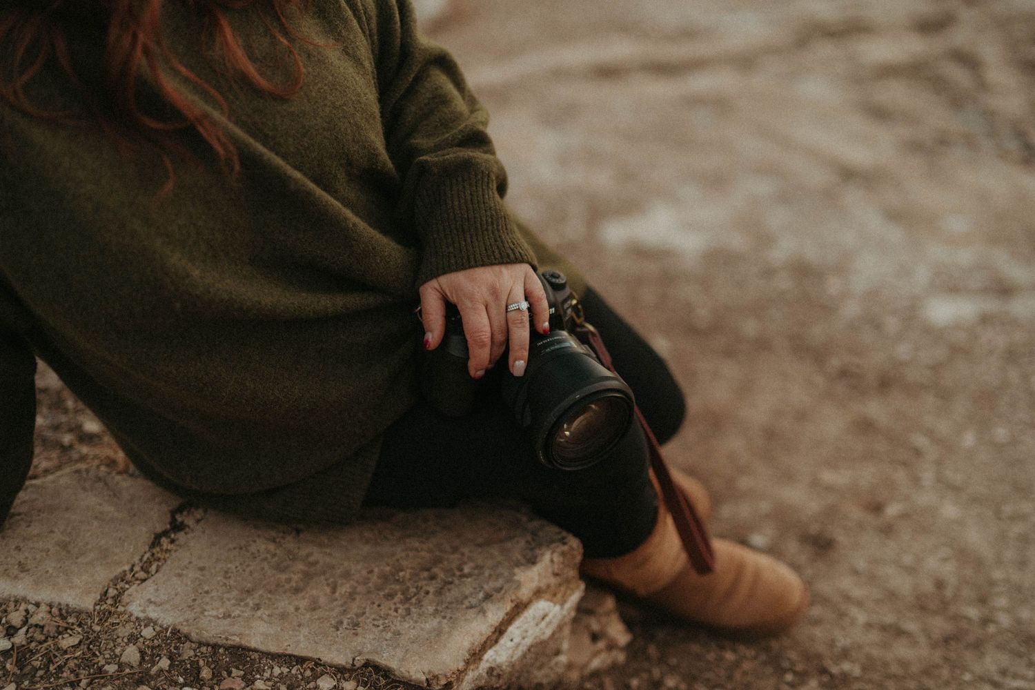 Close-up of a photographer sitting outdoors holding a professional DSLR camera in hand.