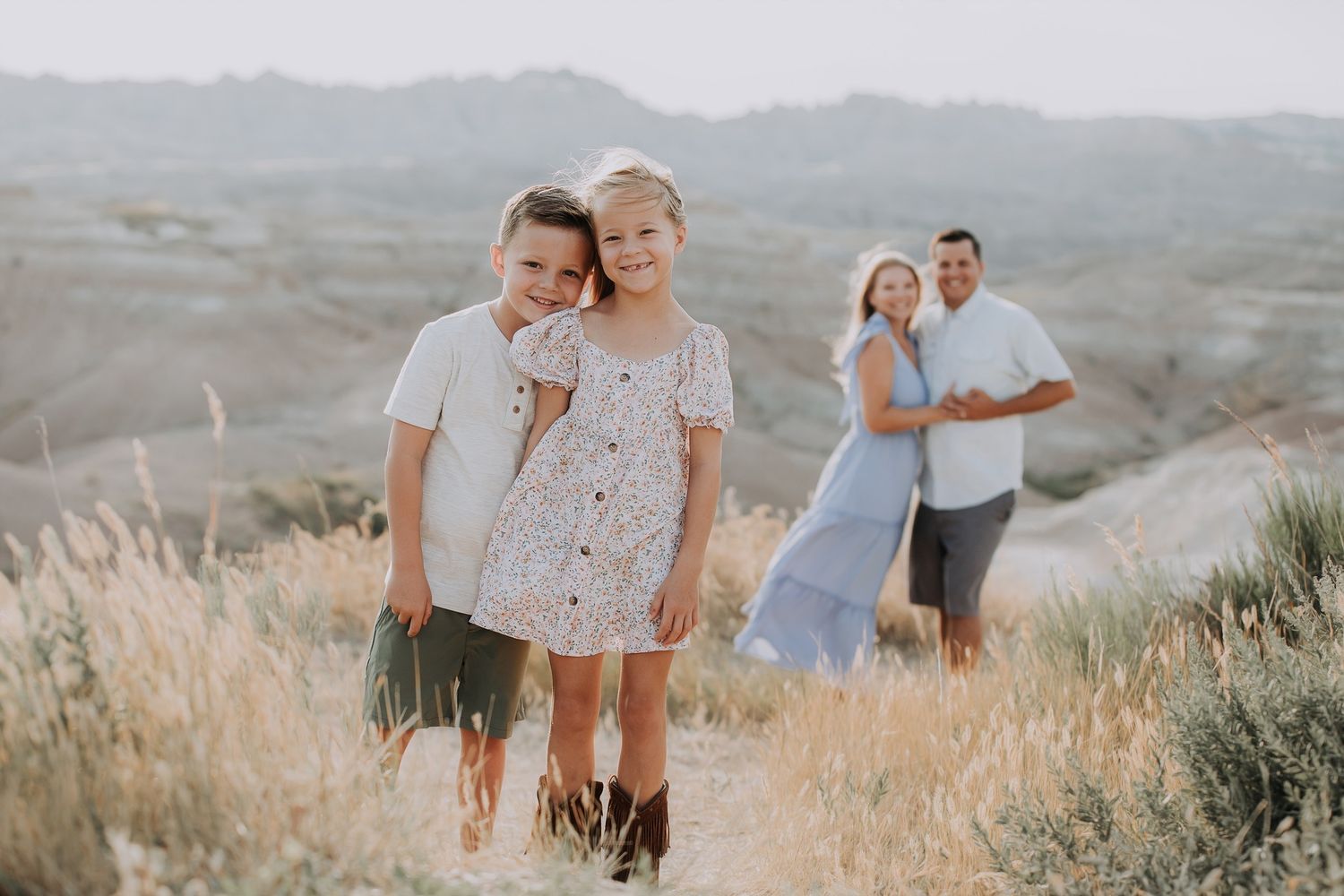 Two siblings posing in front of parents in scenic badlands landscape at sunset.