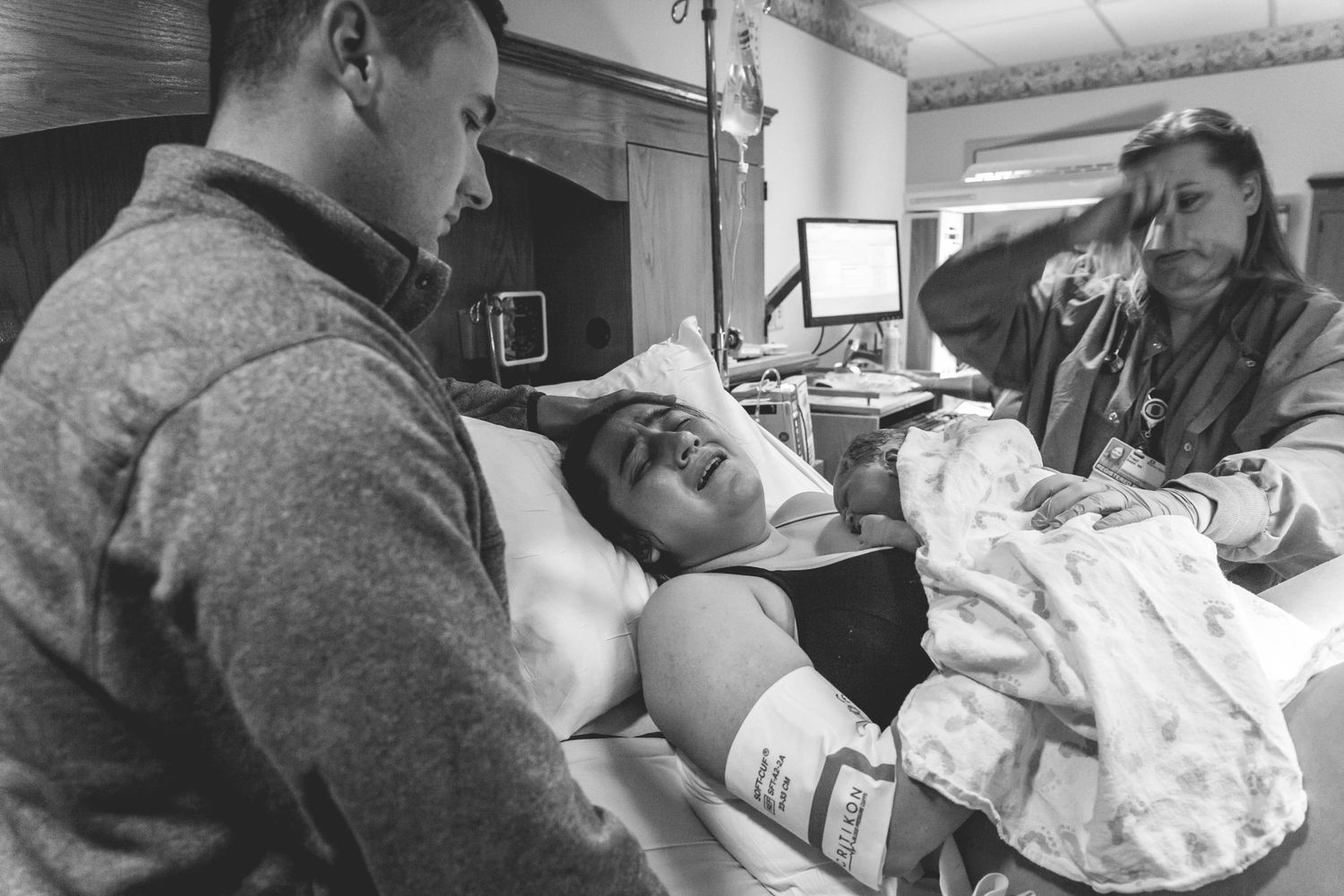 Black and white photo of a woman in labor with support from partner and nurse in hospital room.