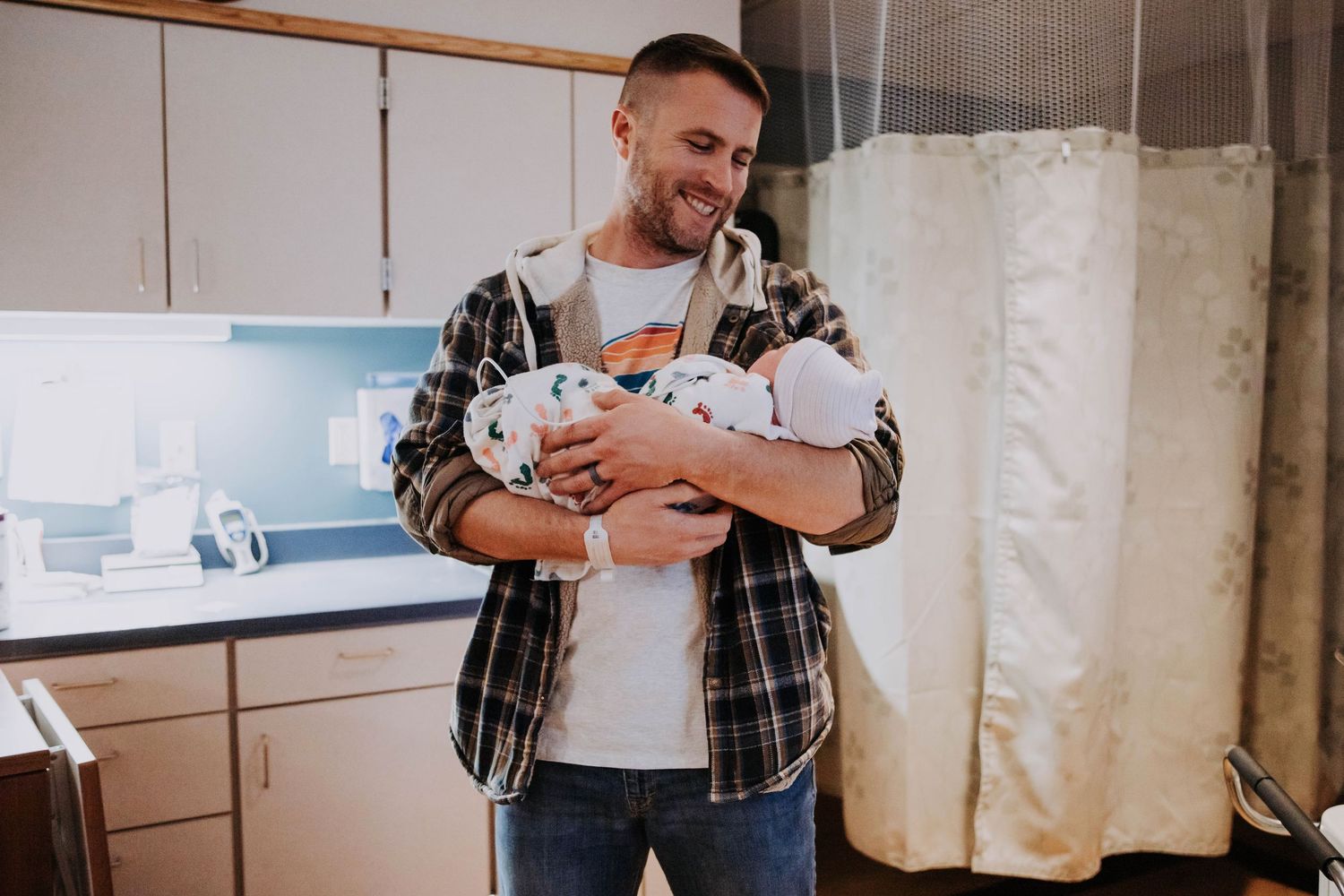 Smiling father holds newborn baby in hospital room after delivery.