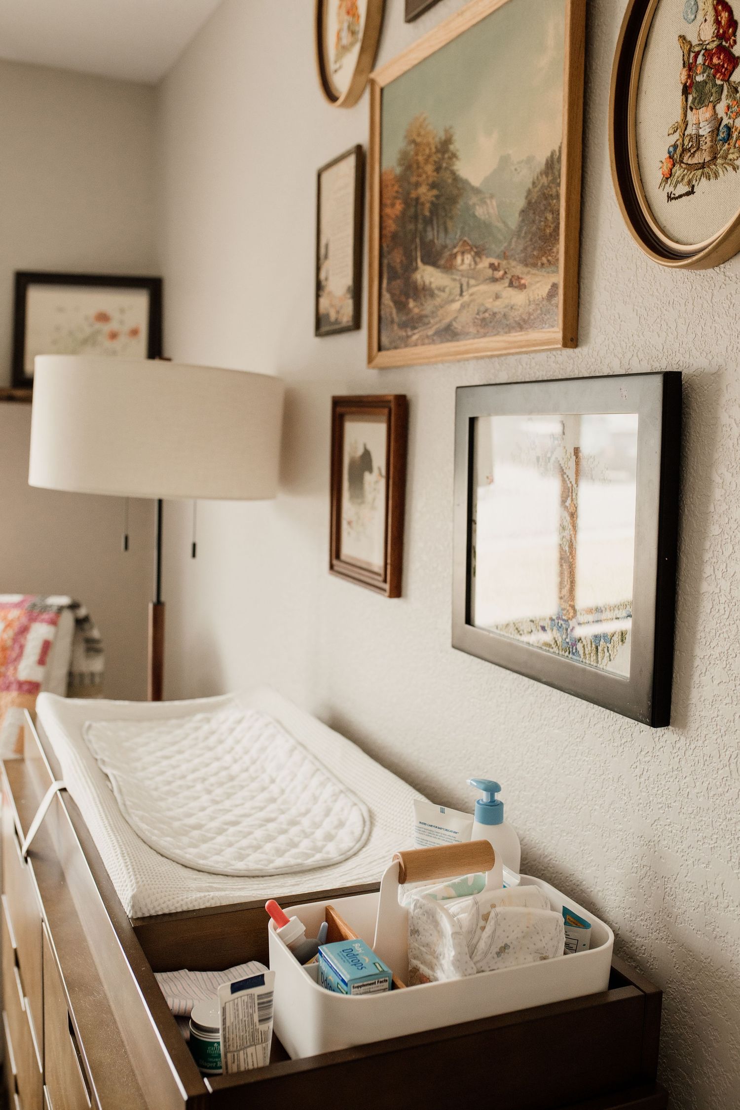 Vintage gallery wall above a baby changing table dresser with organized diaper supplies and a white changing pad.