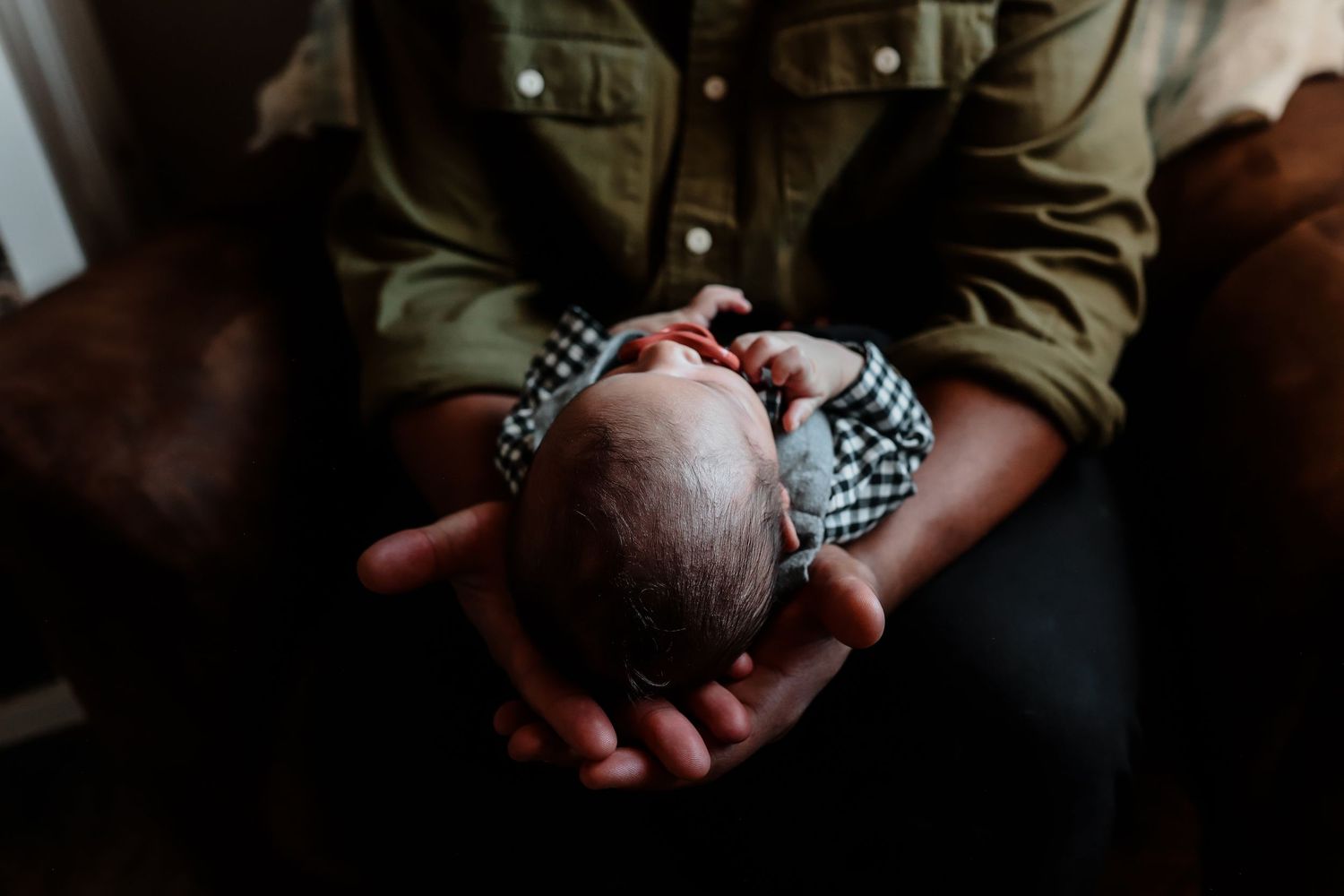 Close-up of fathers hands gently cradling sleeping newborn baby dressed in black and white checkered outfit.
