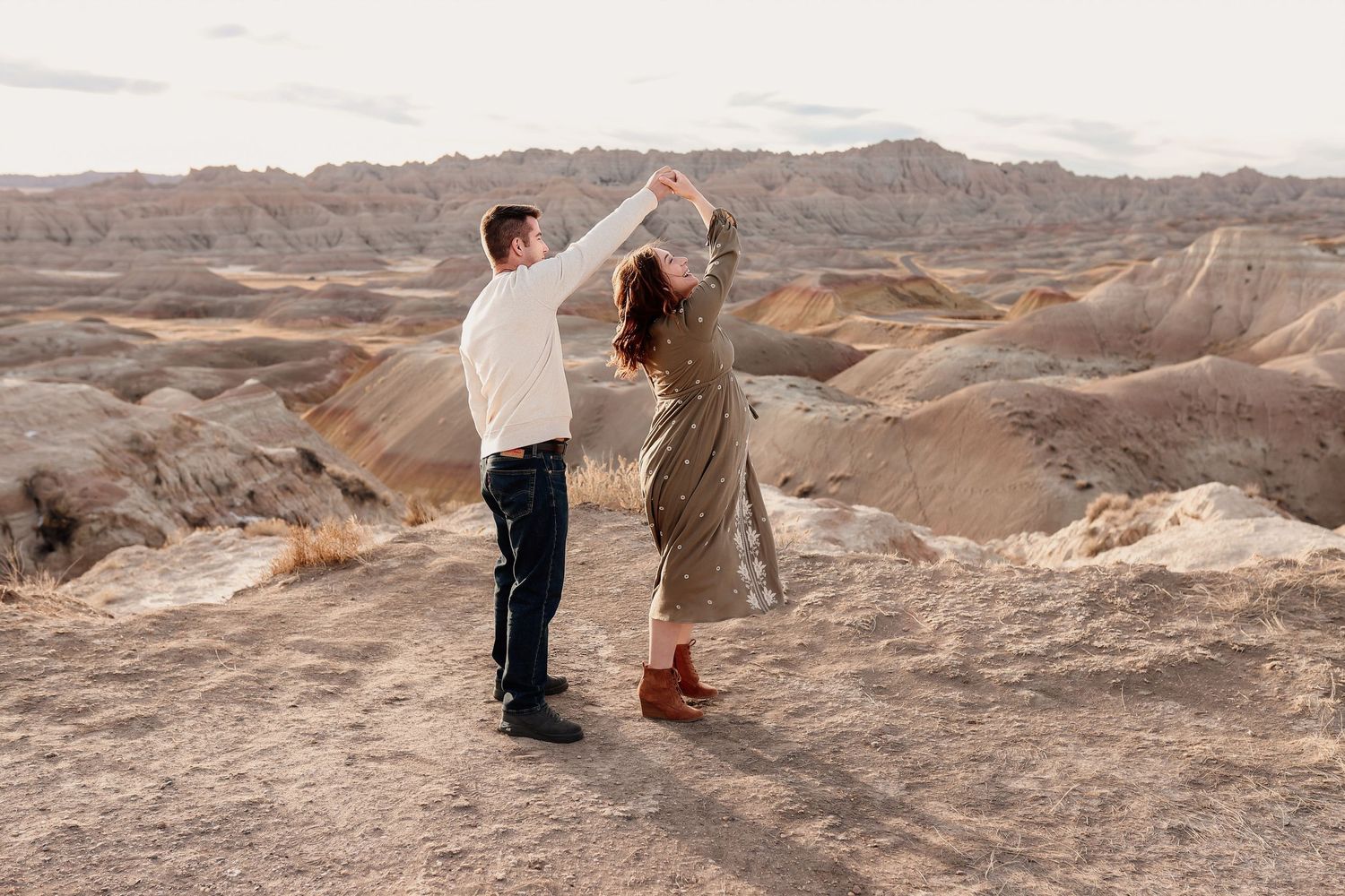 Couple dancing together on rocky badlands terrain at sunset.