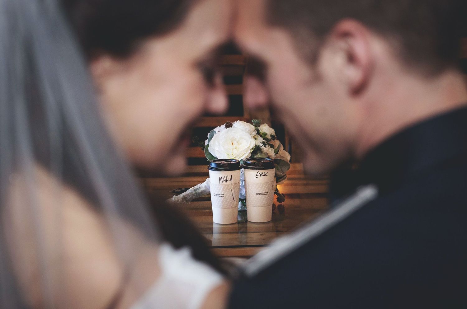 Romantic wedding couple sharing an intimate moment with floral bouquet and candles on wooden table in soft focus.