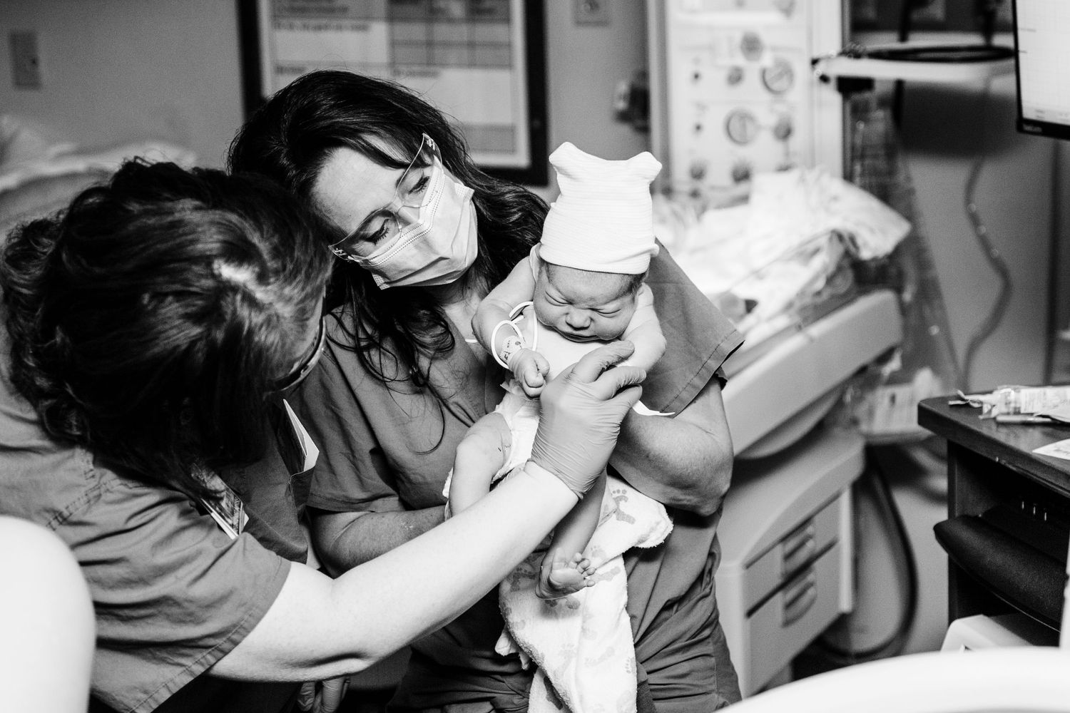 Black and white photo of nurses in masks carefully handling newborn baby in delivery room.