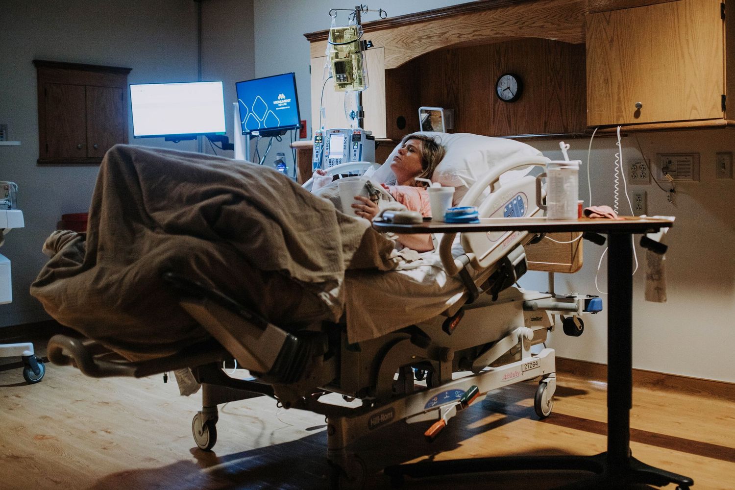 Pregnant woman resting in hospital bed surrounded by medical equipment in a labor and delivery room.