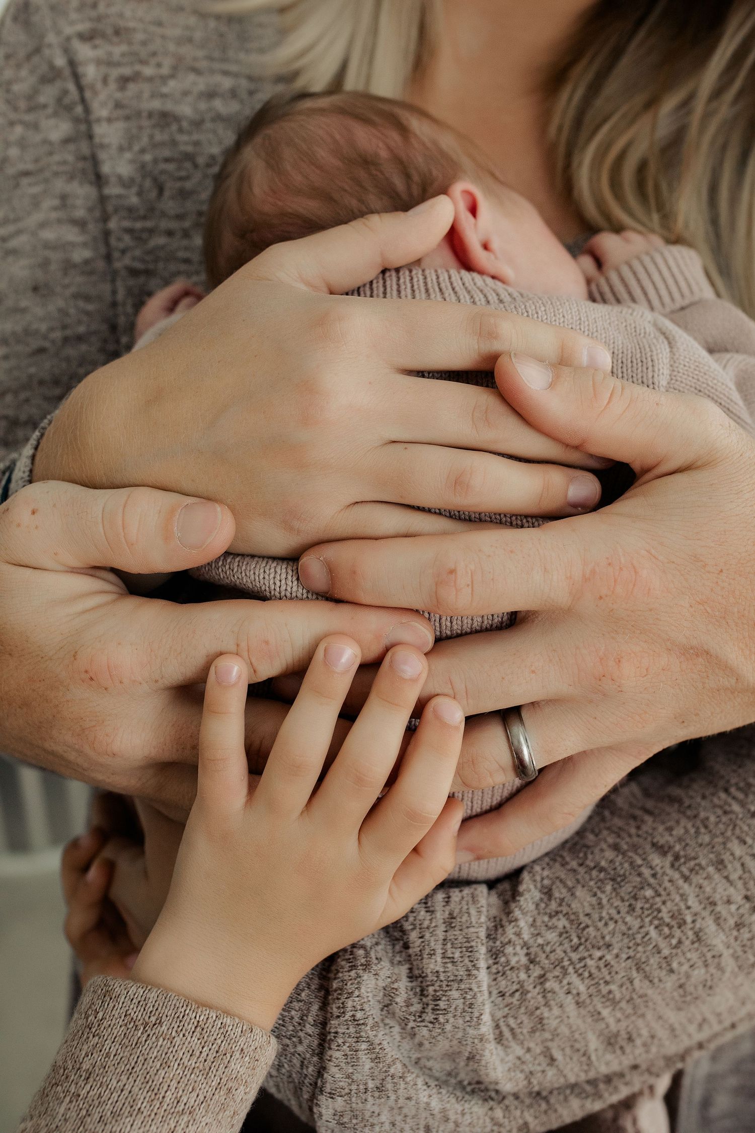 Close-up of multiple hands tenderly cradling a sleeping newborn baby, showing family love and connection.